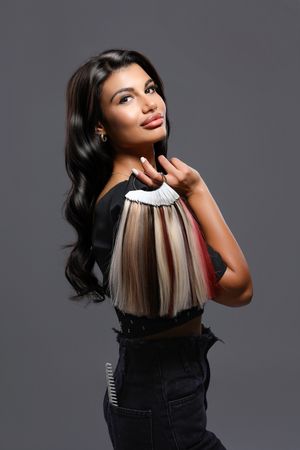 Professional hair styling photo shoot featuring dark hair with contrasting blonde highlights against grey background.