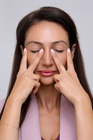 Sequence of someone performing facial massage with hands in pink blouse against light background.