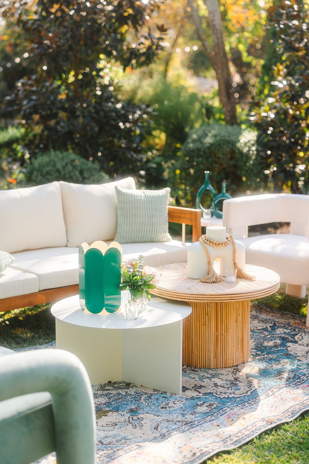 Modern white curved seating arrangement with bamboo coffee tables and turquoise accents on a patterned rug outdoors.