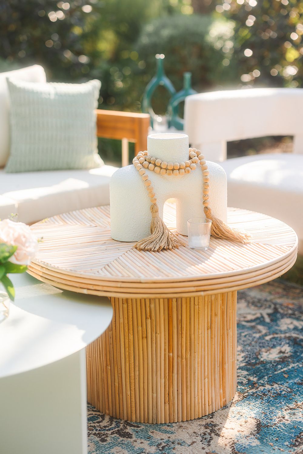 Stylish bamboo coffee table with white ceramic vases and beaded necklace on outdoor patio with white cushioned seating.