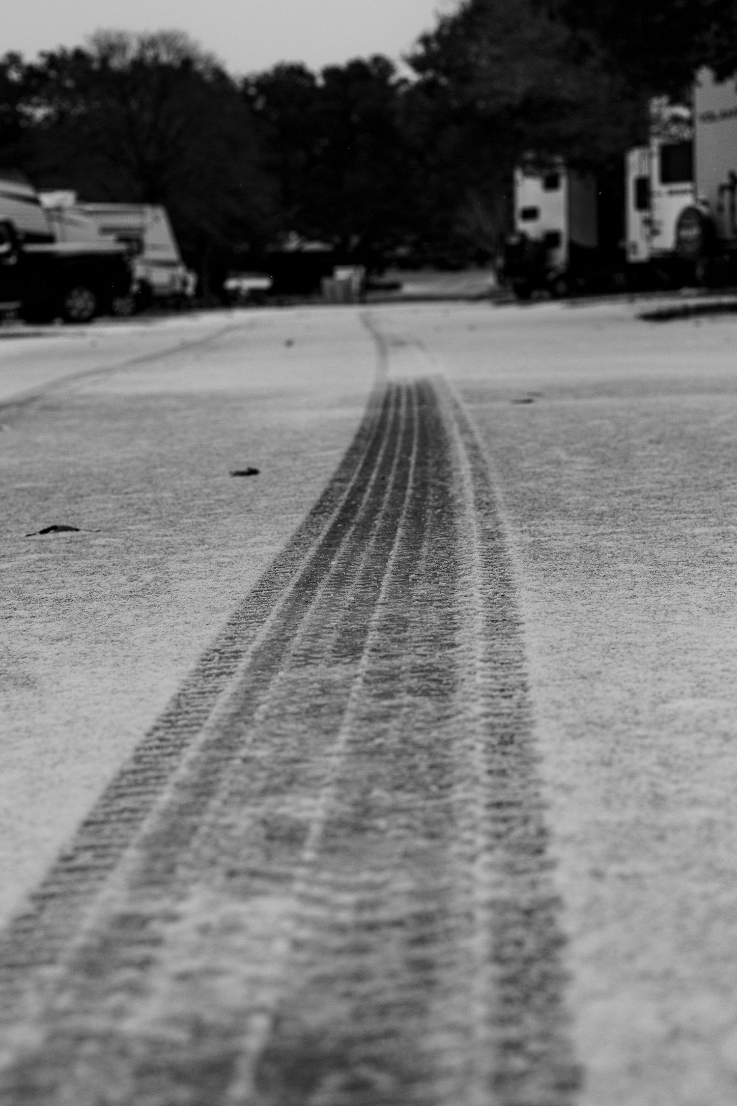 Black and white close-up of tire tracks on a snowy surface creating parallel lines leading into the distance.