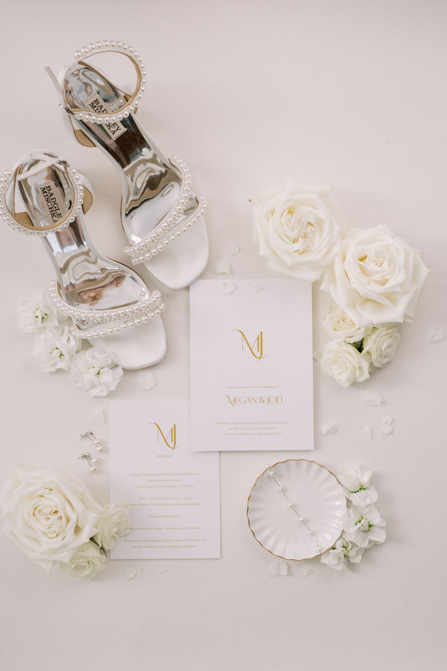 Elegant white and gold wedding stationery with roses and delicate details arranged on light gray background.