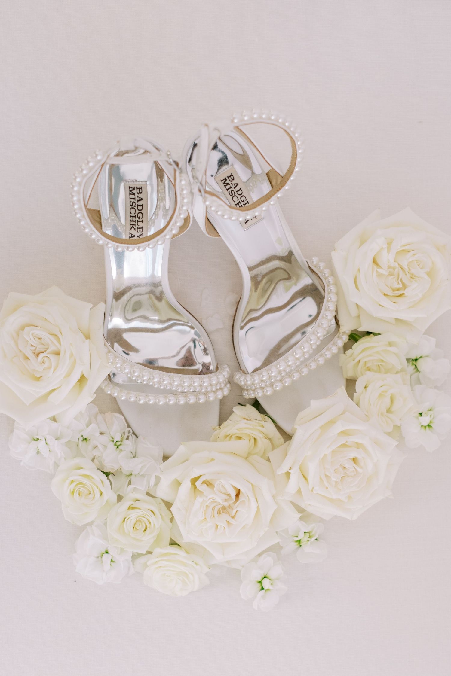 White bridal shoes and roses styled with pearl details on light neutral background.