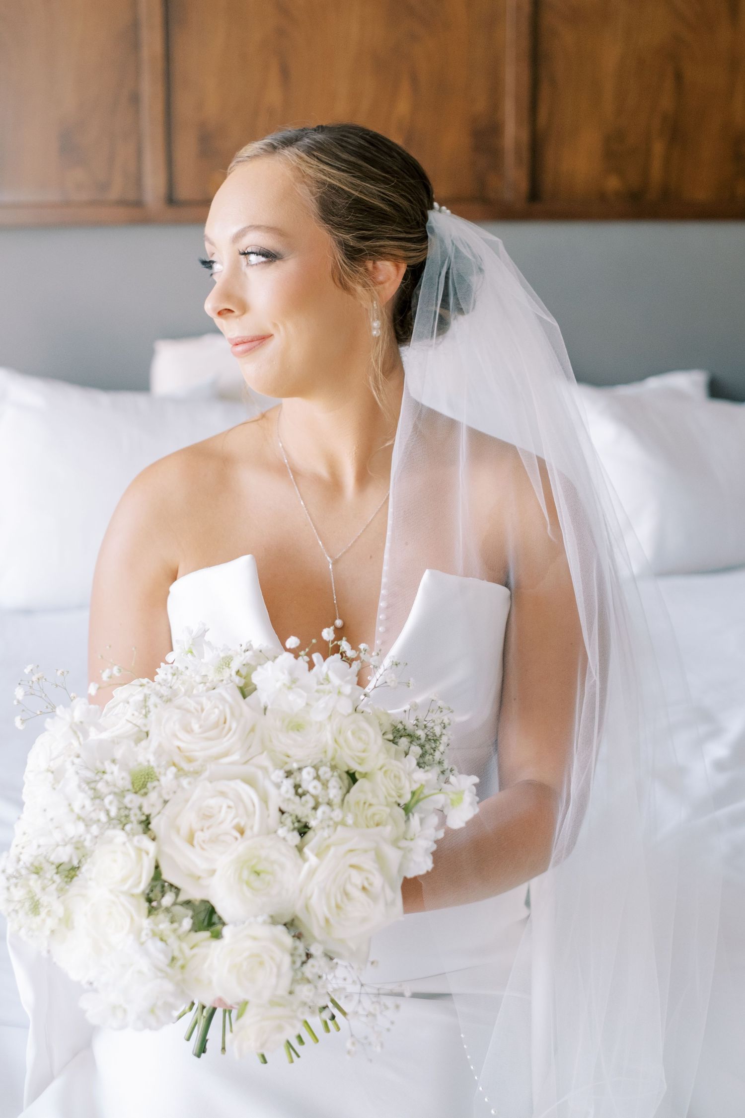 Stunning white bridal bouquet held against soft white bedding in natural light.