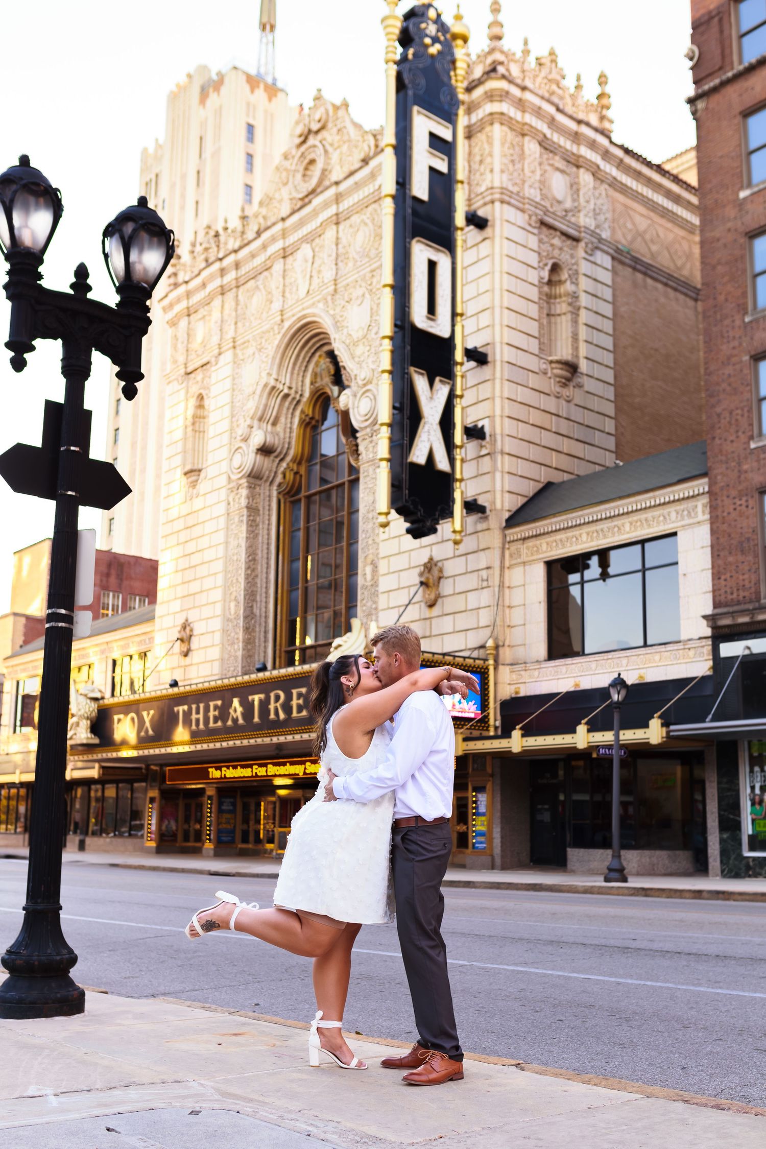 Dancing couple performs dramatic dip pose in front of historic brick building with street lamps.