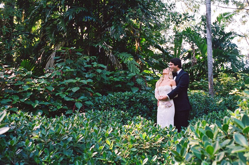 A couple dances together in a lush green garden setting surrounded by tropical foliage and natural lighting.