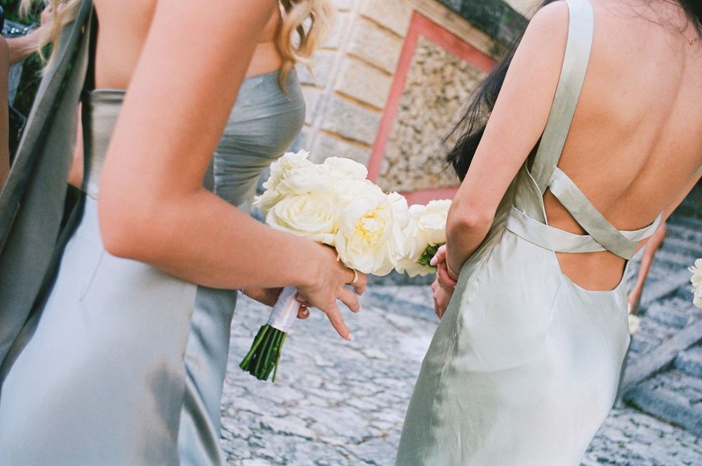 Bridesmaids in pale blue dresses hold white rose bouquets during an outdoor wedding ceremony.