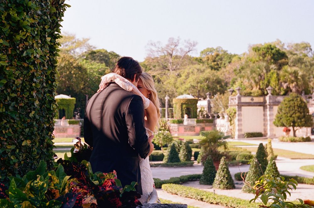 A couple embraces in a peaceful garden cemetery surrounded by headstones and evergreen shrubs on a sunny afternoon.