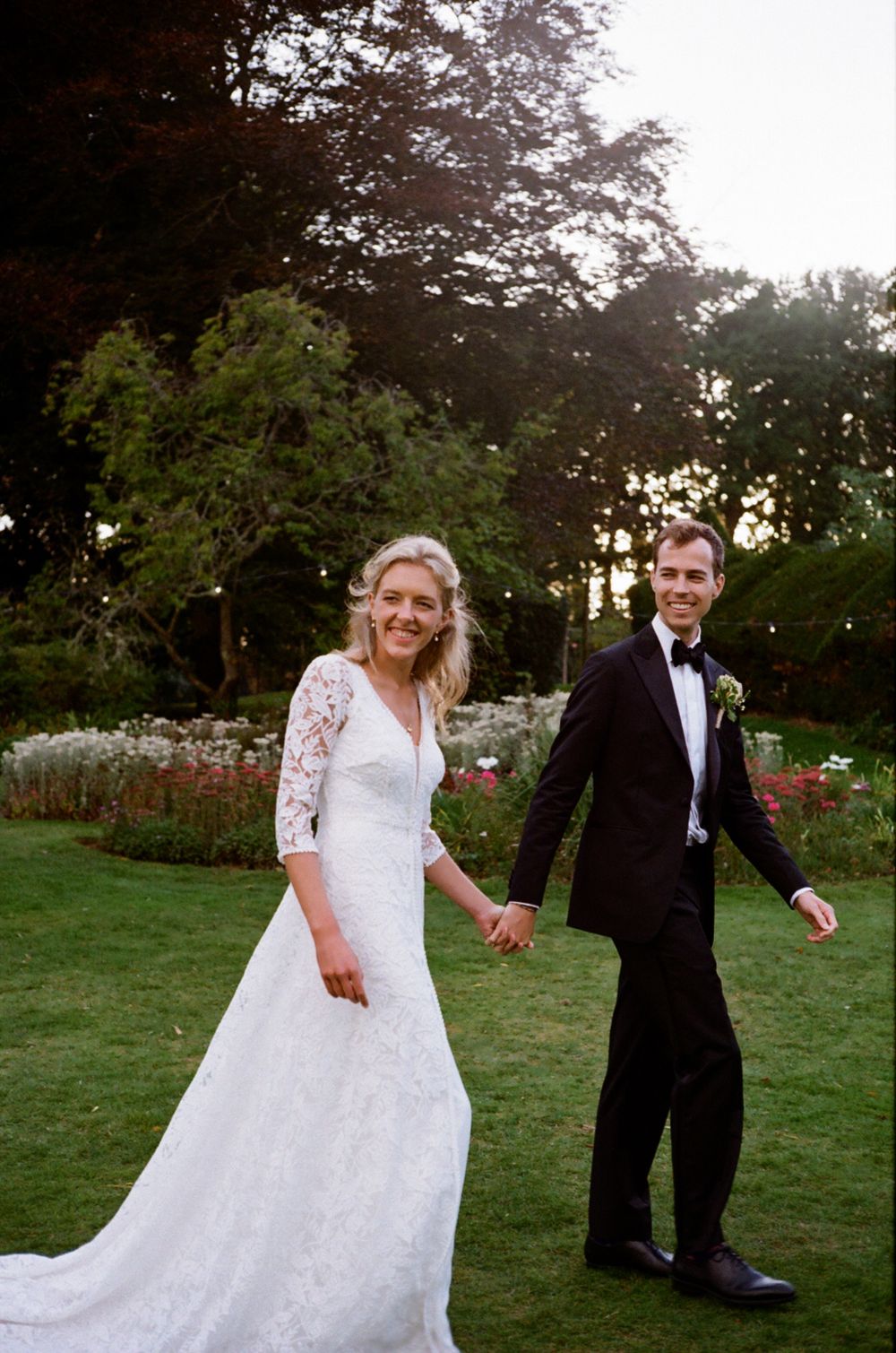 Bride & groom walking and smiling away from camera whilst holding hands.