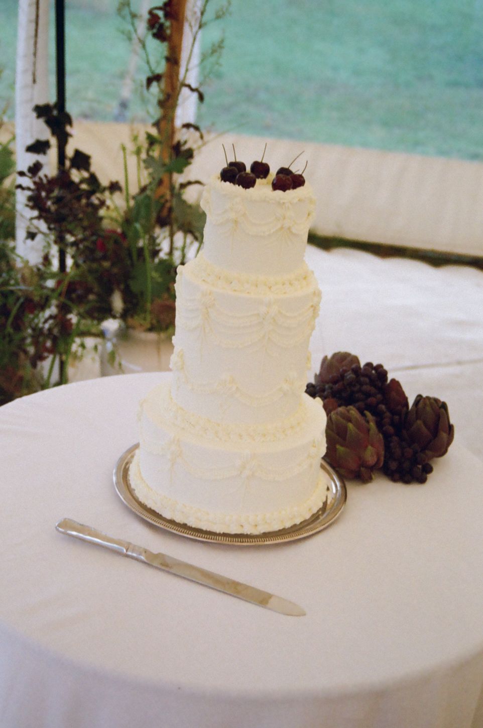 Wedding cake & knife on a table decorated with fruit garnishes including cherry