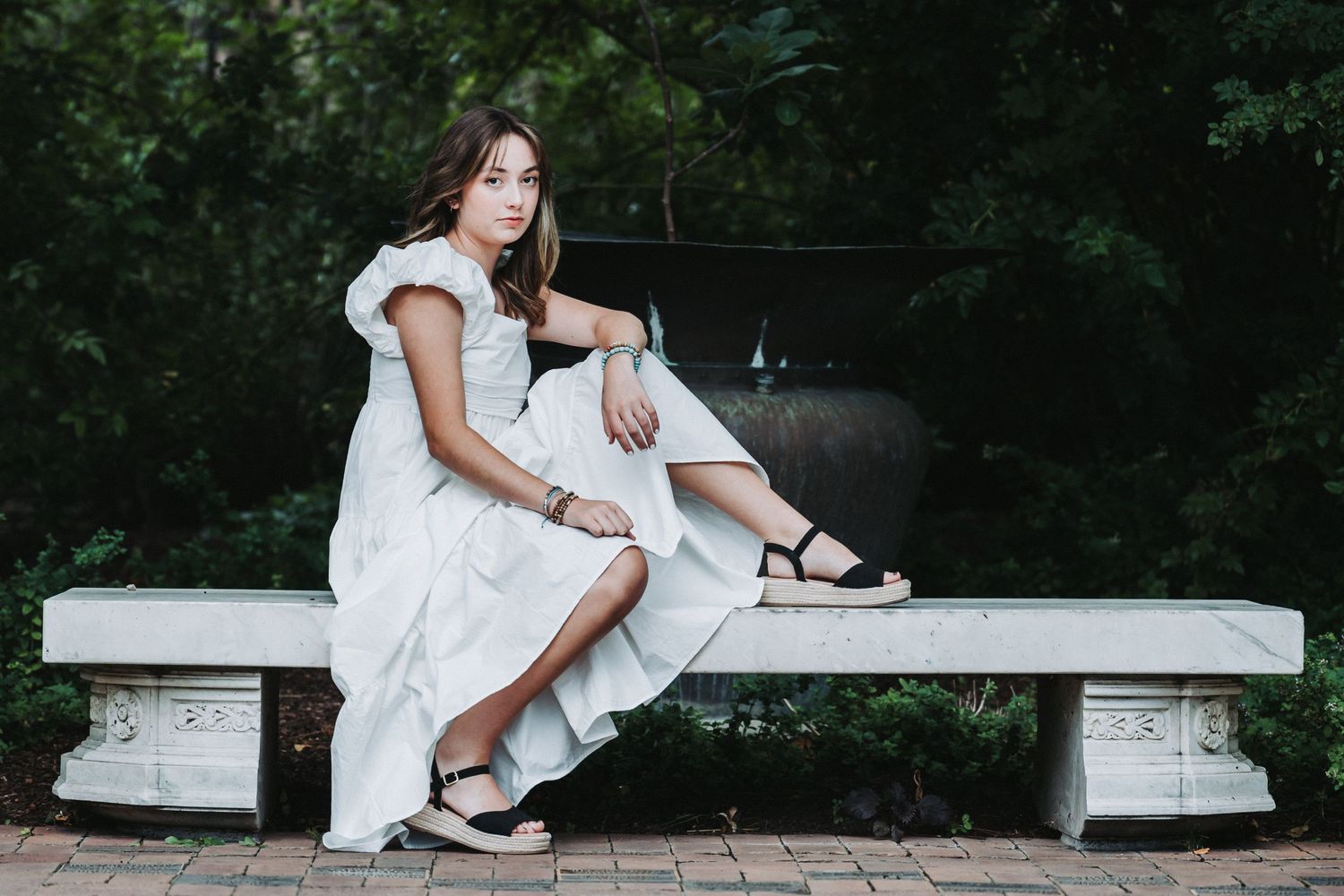 Person in white dress resting on stone bench in garden setting.