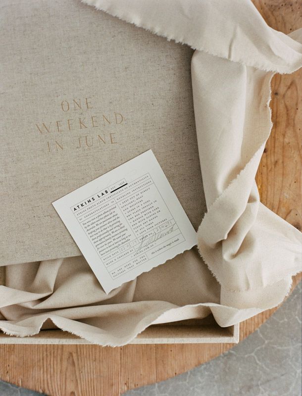 A linen fabric with text reading 'One Weekend in June' next to a white paper card on wooden surface.