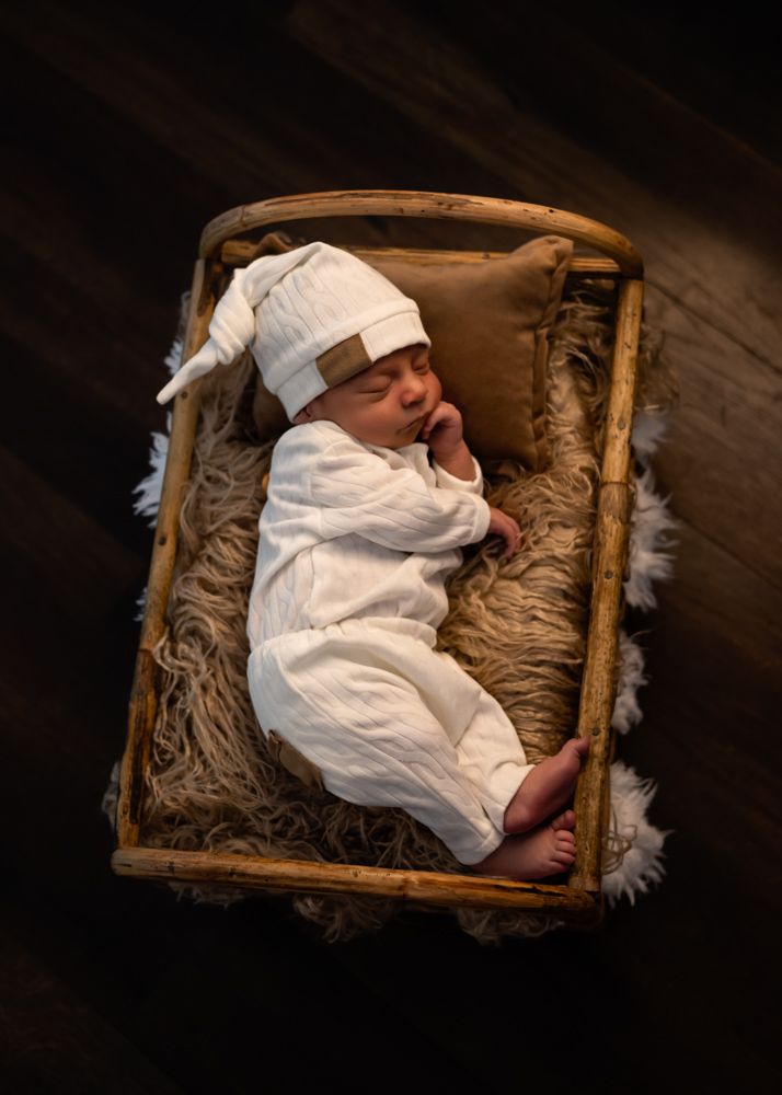Black and white photo of a sleeping newborn baby wrapped in a knit blanket inside a rustic wicker basket.