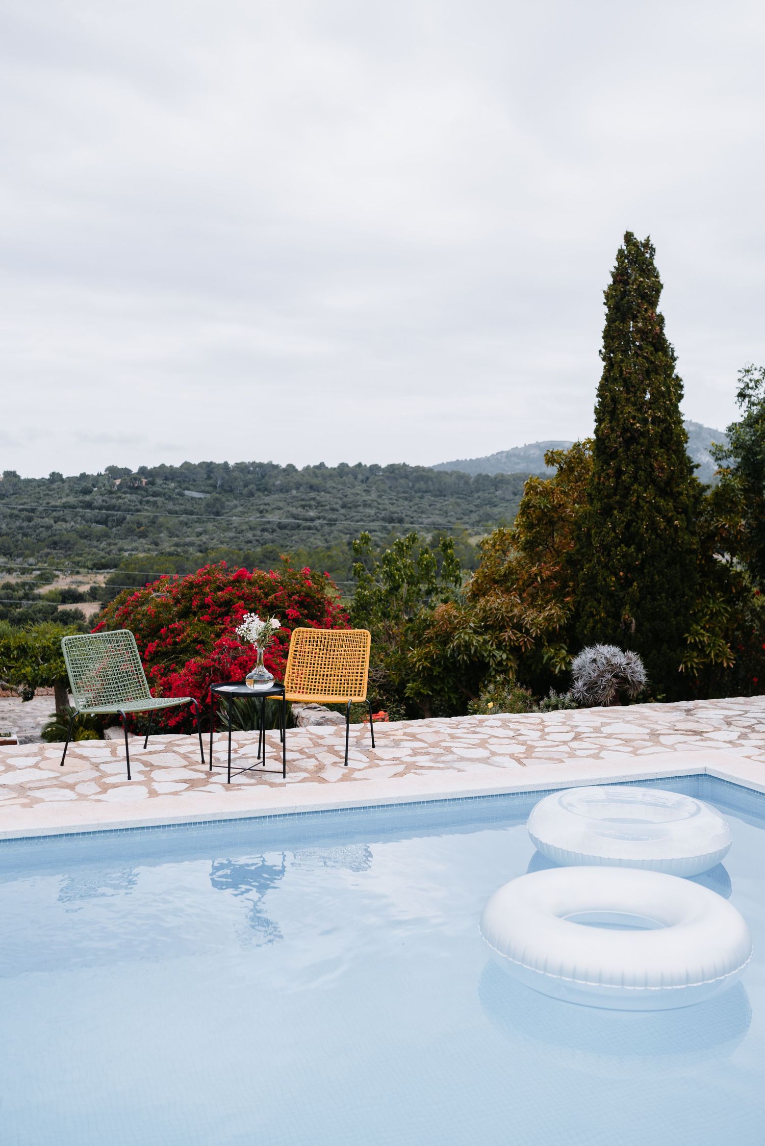 Poolterrasse mit bunten Stühlen und weißen aufblasbaren Schwimmreifen mit Blick auf die malerische Berglandschaft Mallorcas auf der Finca.