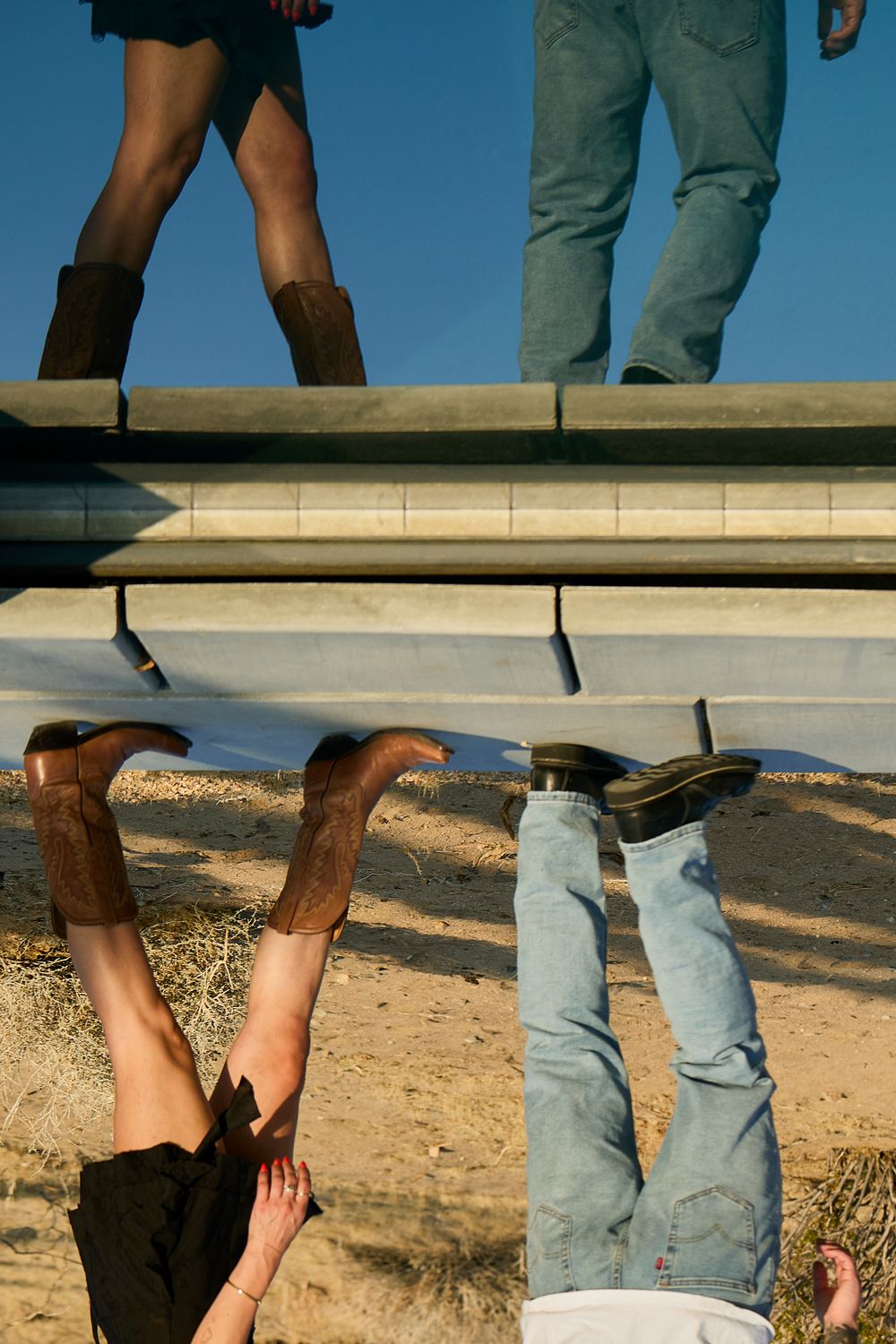 Legs and feet of people standing on a white ledge or platform against a desert landscape.