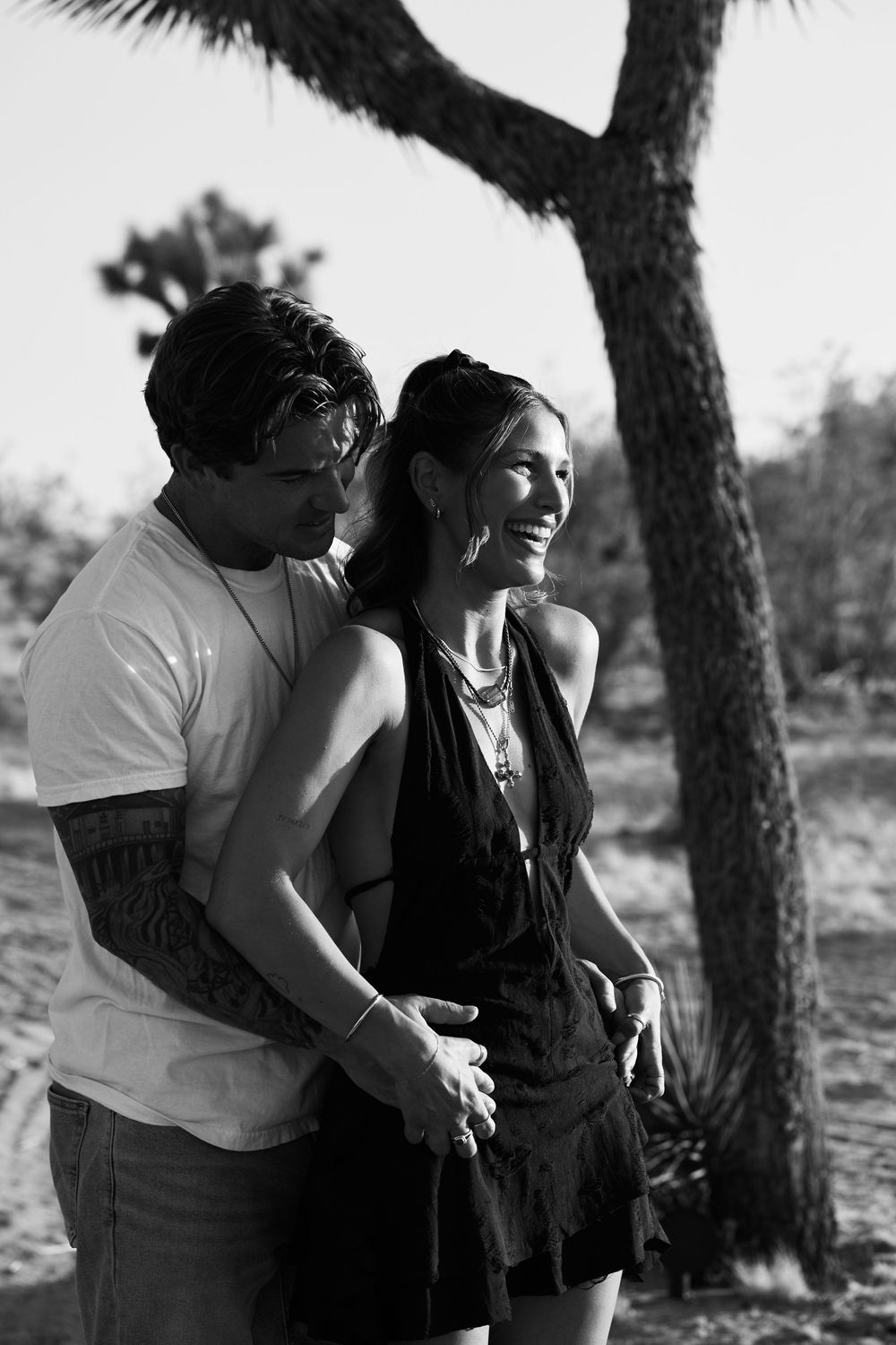 A black and white photo of a couple sharing a tender moment outdoors under a tree.