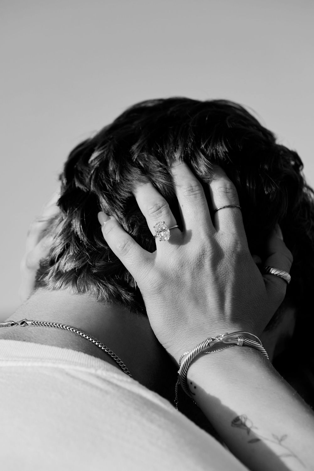 Black and white photo showing a hand with rings and bracelets running through dark hair in a moody composition.