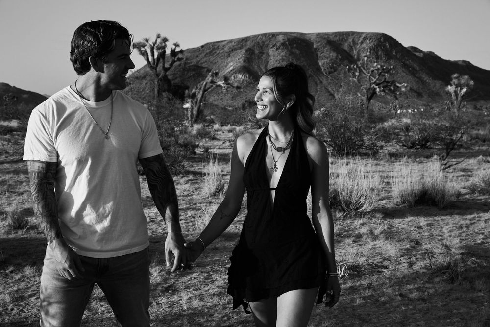 A couple shares a joyful moment while walking together in a rocky desert setting with mountains behind them.
