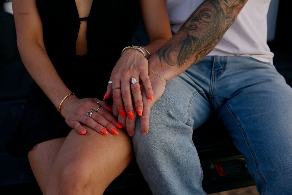 Close-up shot of couple sitting together with woman wearing red nails resting hands on leg.
