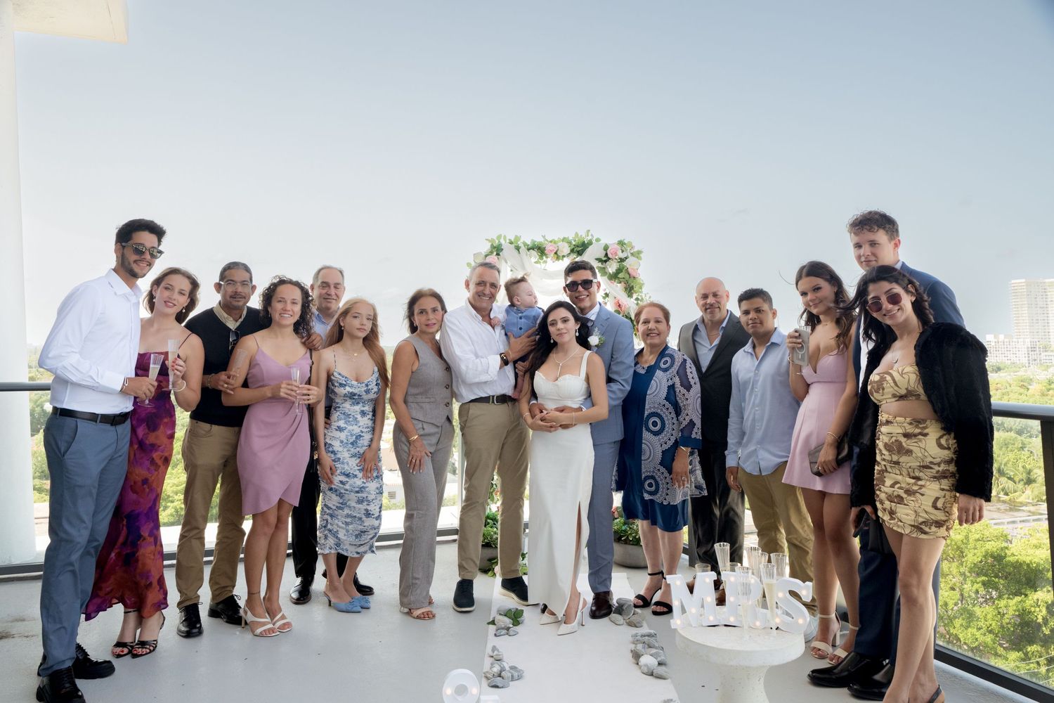 Wedding party lineup against blue sky background along oceanfront beach setting with palm trees and decor.
