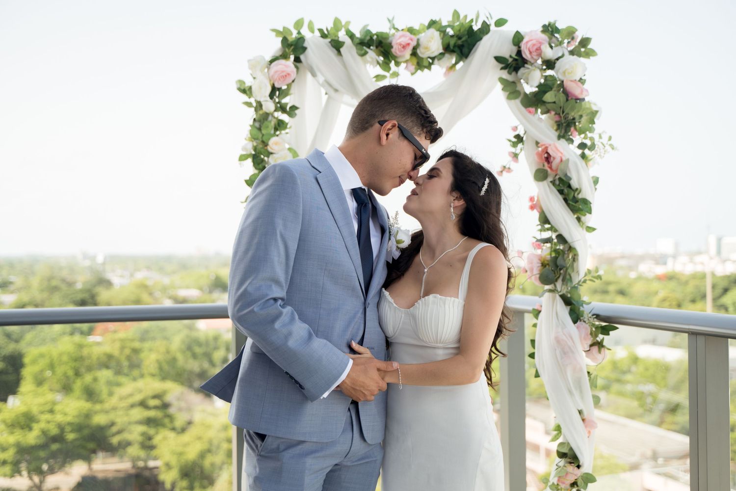 A romantic wedding ceremony moment captured on a balcony decorated with pink and white floral arrangements.