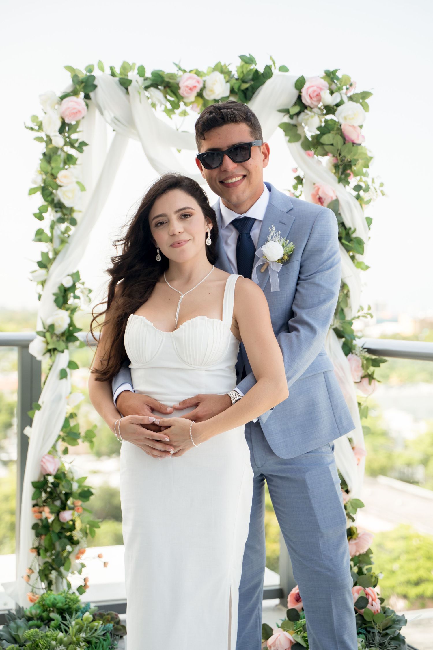 A couple shares a romantic moment under a floral arch at their outdoor wedding ceremony.