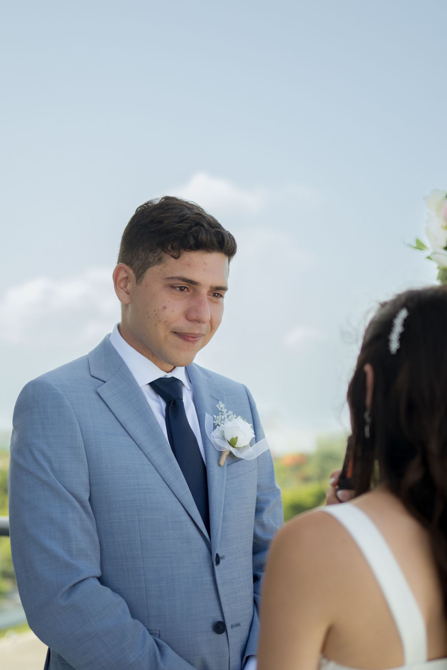 A wedding ceremony on a rooftop terrace with a couple sharing an emotional moment under a blue sky.