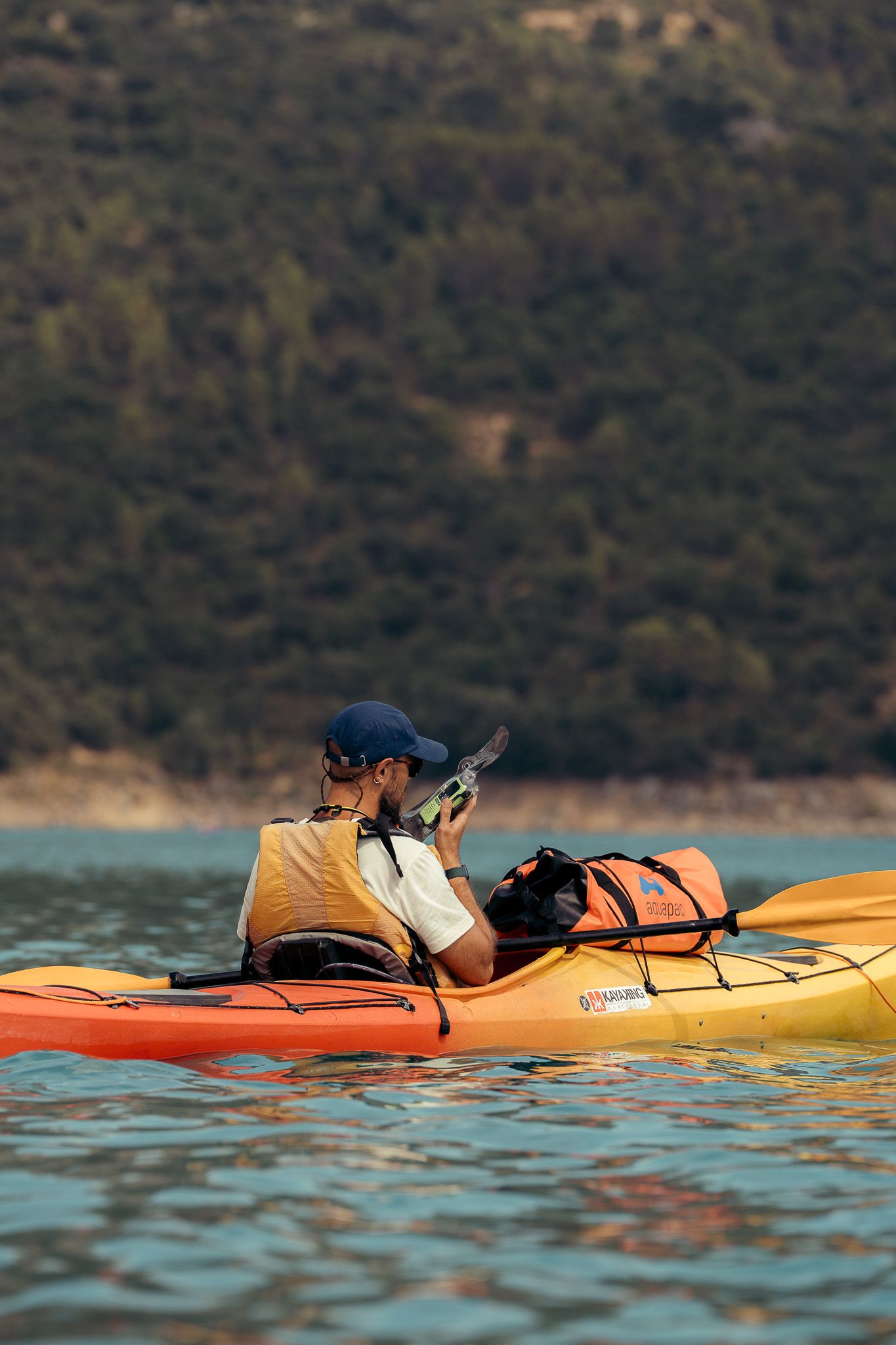 Orange and yellow kayak floating on calm water with mountainous terrain in background.