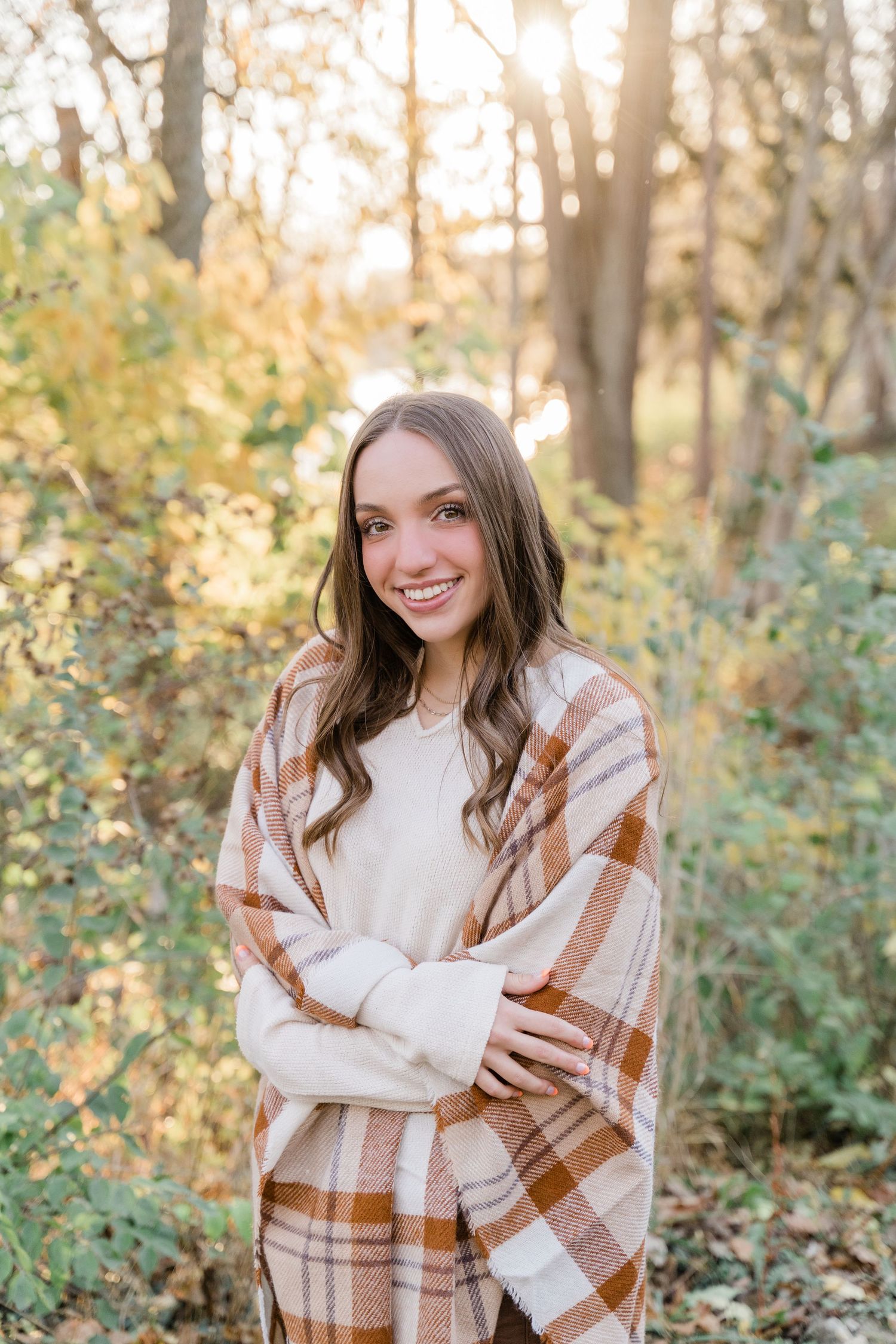 A warm autumn outdoor portrait featuring a person wearing a cozy plaid scarf and cream sweater in a sunlit wooded setting.