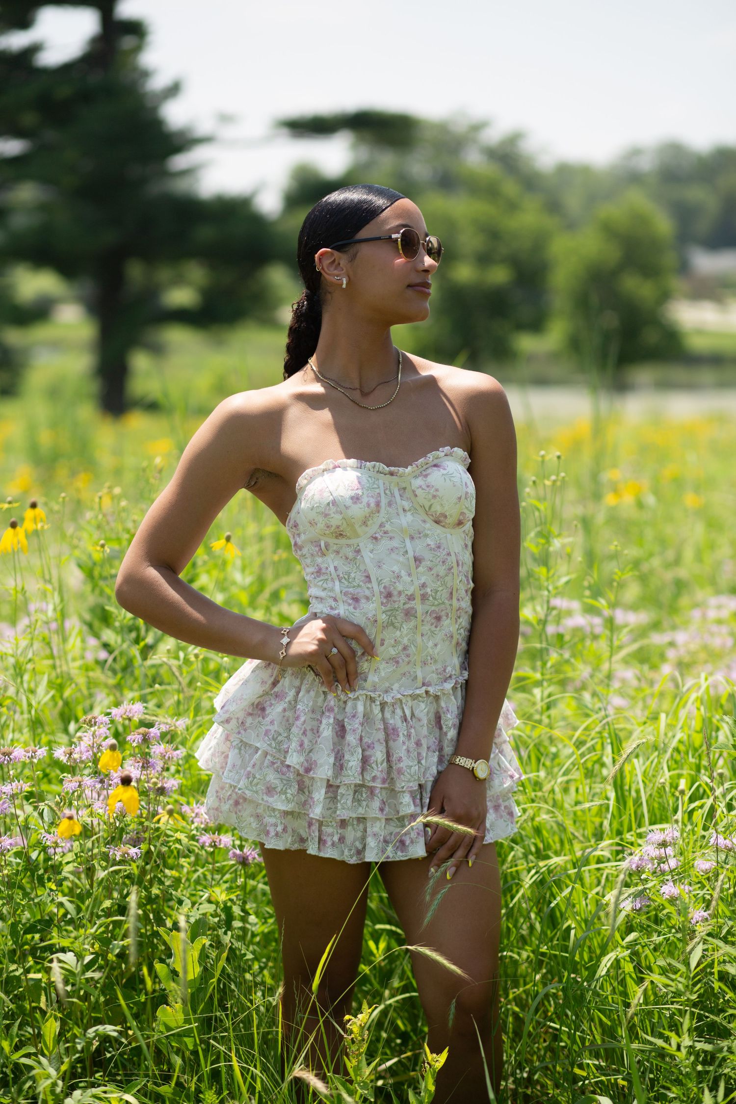 A person in a floral white top poses gracefully in a sunny wildflower meadow.