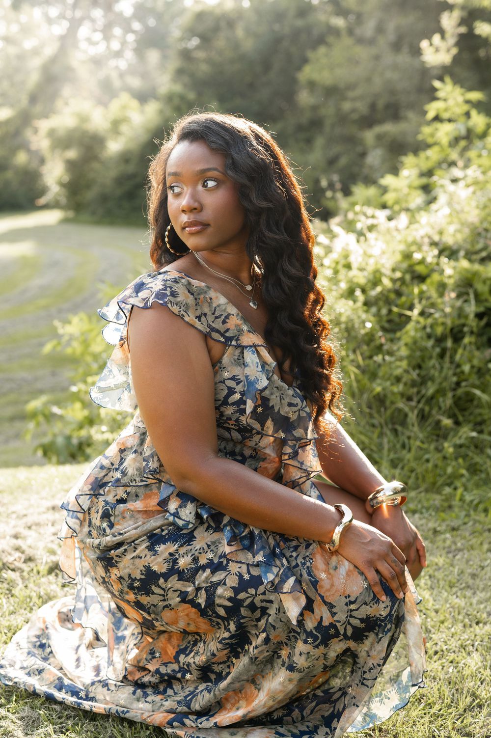 A person in a floral dress poses gracefully on grass during golden hour sunset lighting.