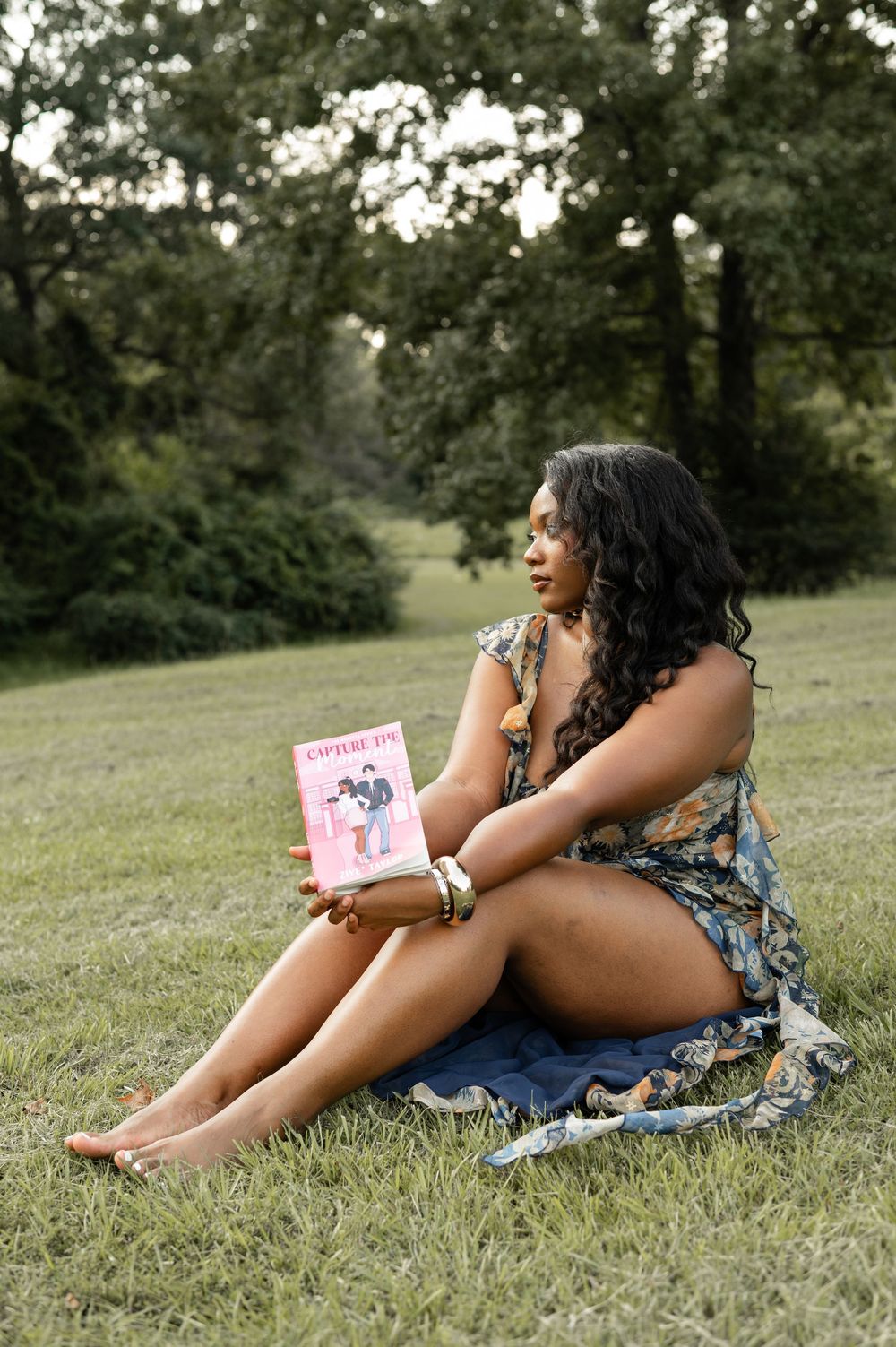 Someone relaxing on grass holding up romance novels while wearing floral top and denim shorts.
