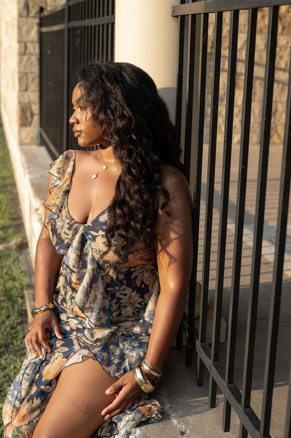 A woman in a floral dress poses next to a wrought iron railing during golden hour sunlight.