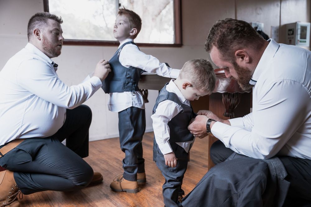 Two pairs of people in formal wear helping each other prepare and adjust their outfits before an event.