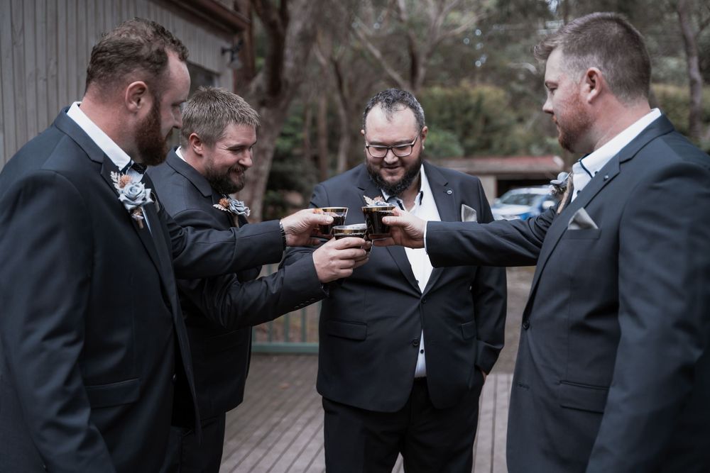 A group of groomsmen in black suits laughing and looking at something on their phones during a wedding celebration.