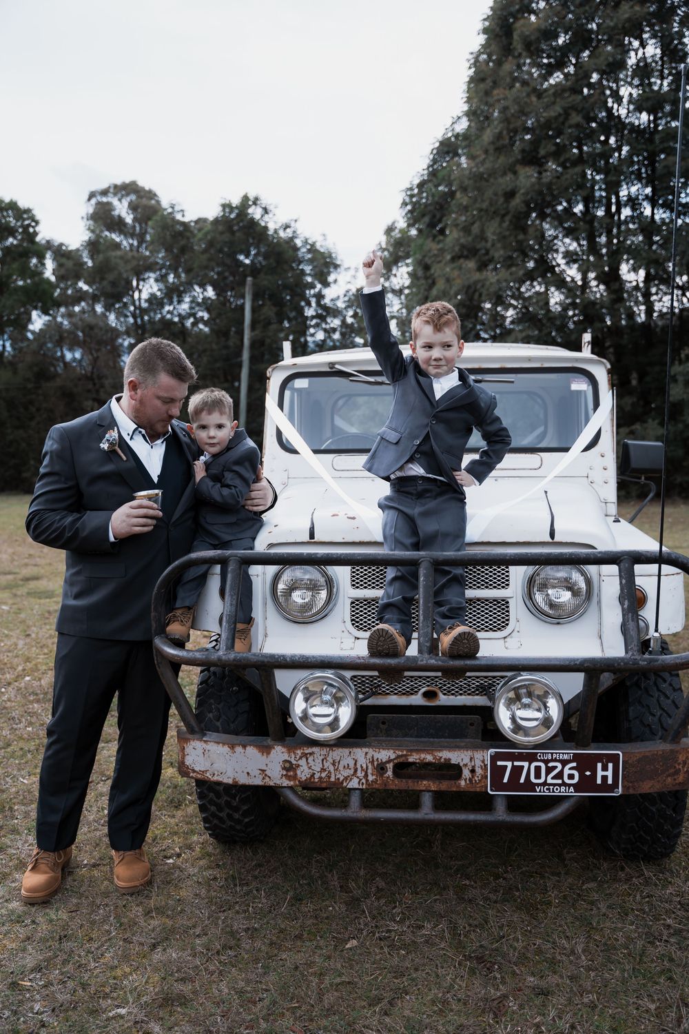 A classic white vintage truck with rustic charm being used as a casual photo backdrop in a wooded outdoor setting.