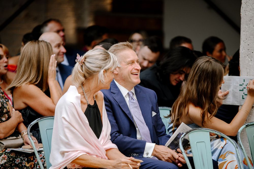Wedding guests sit at elegant outdoor reception tables sharing smiles and conversation in a joyful celebration.