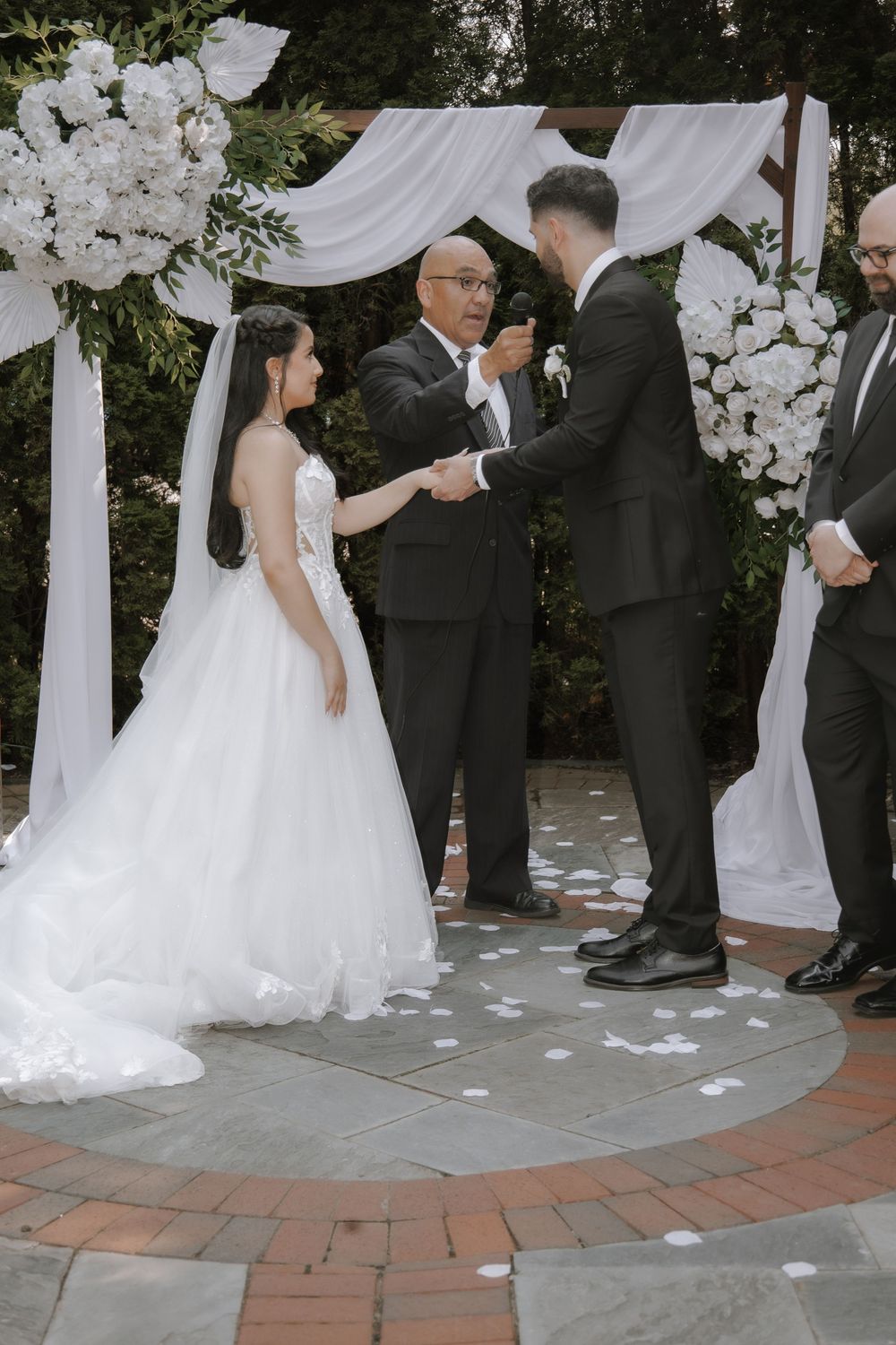 Wedding ceremony sequence shows white petals scattered on brick pavers while attendees in formal attire gather at outdoor venue.