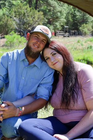 Young couple sitting closely together smiling in a sunny outdoor rural setting.