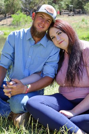 Young couple sitting in grass by a pond, woman resting head on mans shoulder, holding hands outdoors.