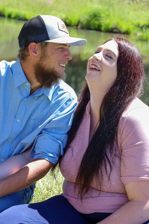 Happy couple laughing together while sitting outdoors near a pond on a sunny day.