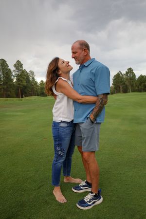 Romantic middle-aged couple embracing on a lush green golf course under a cloudy sky.