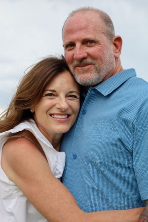 Happy middle-aged couple hugging closely outdoors, woman smiling brightly at the camera.