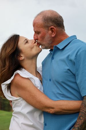 Middle-aged couple sharing a romantic kiss while embracing on a green golf course outdoors.