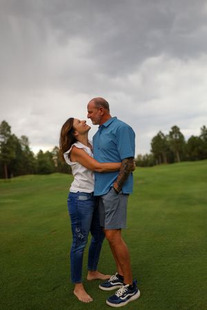 Middle-aged couple holding each other close on a lush green golf course under cloudy skies.