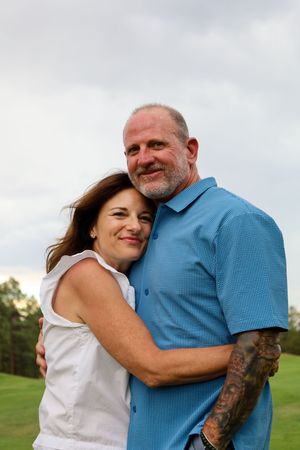 Smiling middle-aged couple embracing warmly on a golf course with trees in the background.