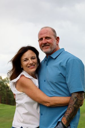 Happy middle-aged couple hugging and smiling on a green golf course under an overcast sky.