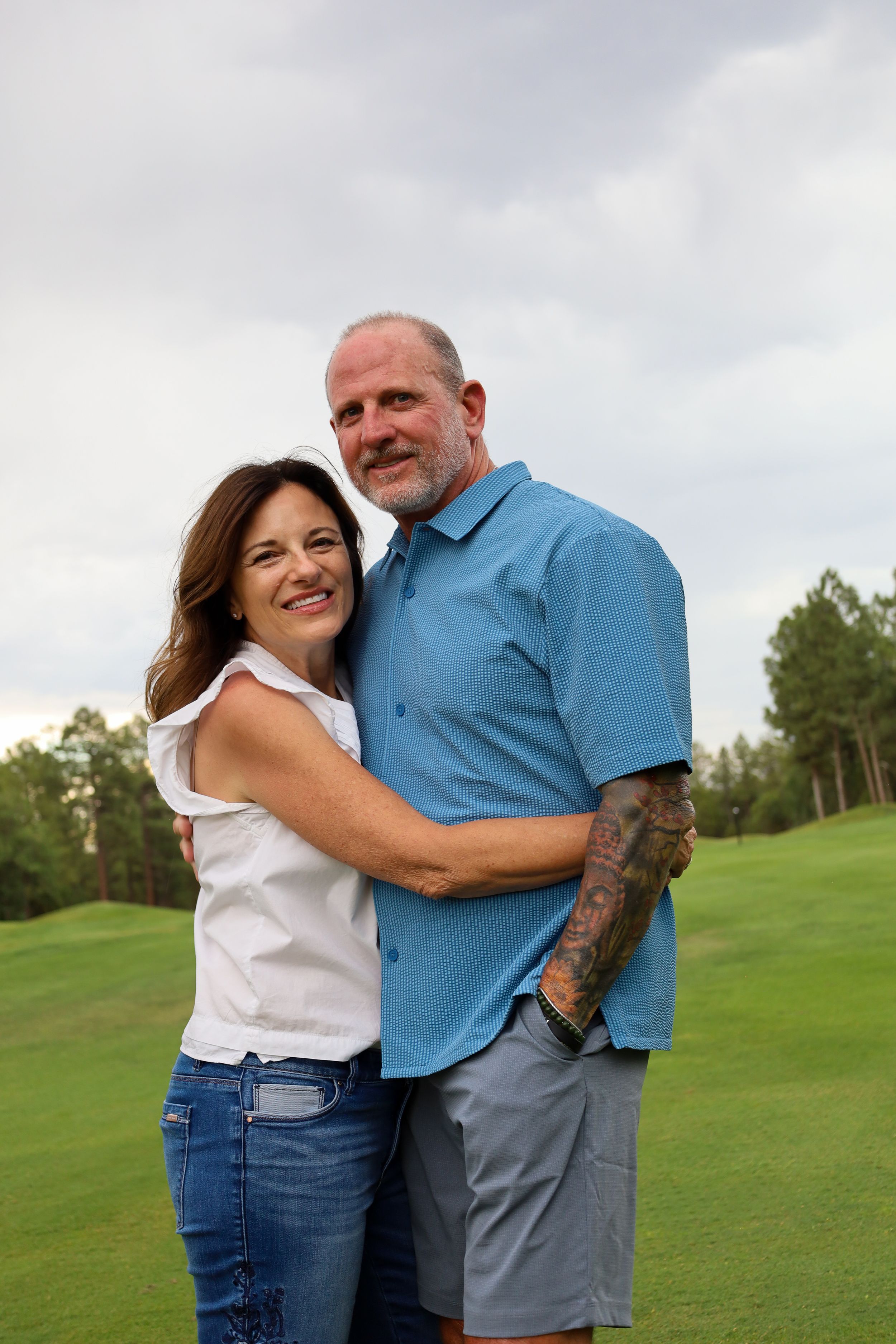 Affectionate middle-aged couple embracing and smiling together on a lush green golf course.