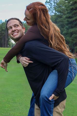 Laughing woman getting a piggyback ride from smiling man on a lush green golf course.