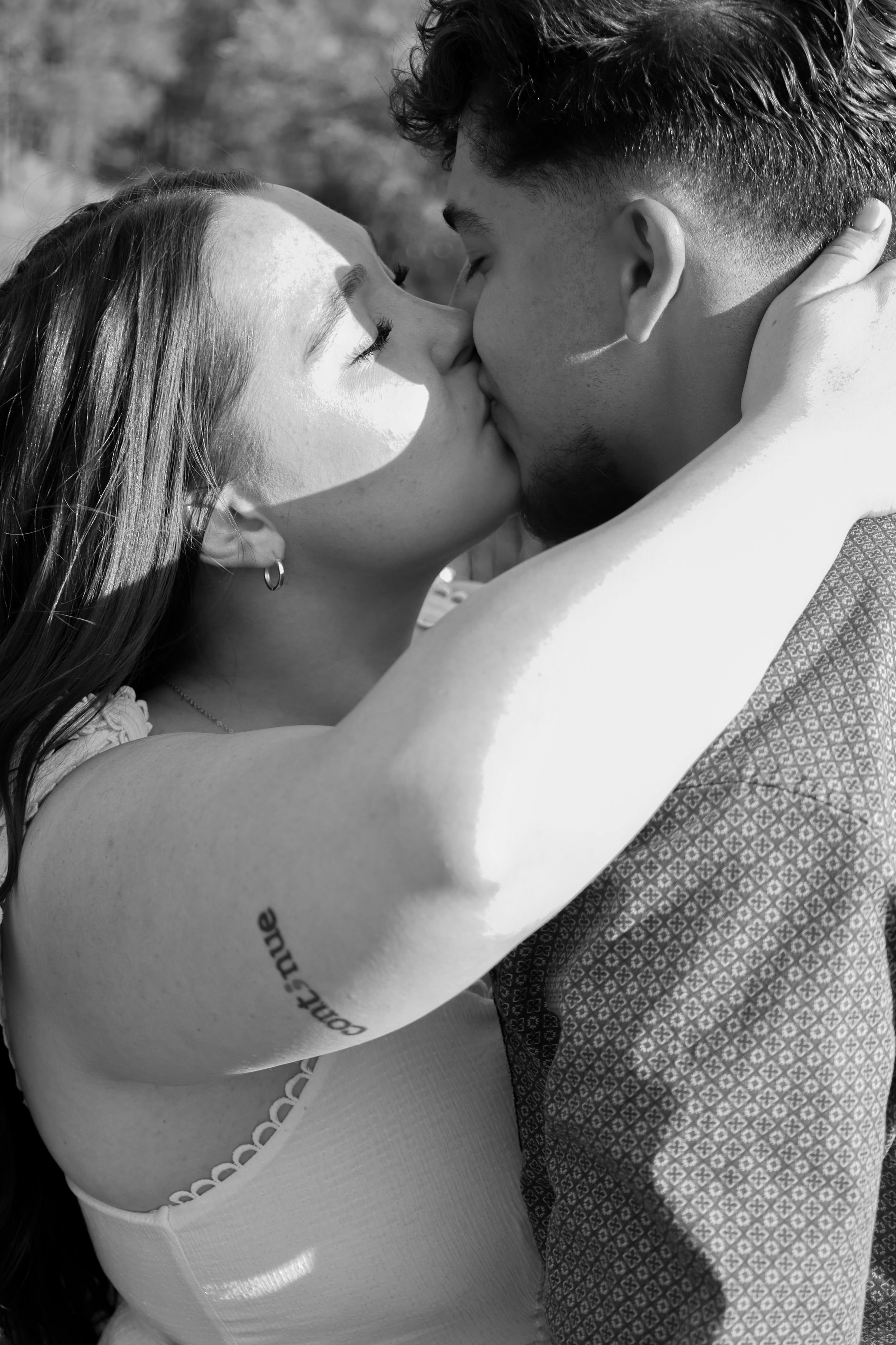 A young couple shares a kiss outdoors in a romantic black and white portrait photo.